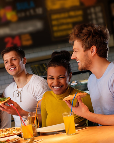 Group of 4 young people eating pizza at a restaurant