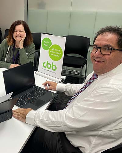 Mark Gauci sitting at a table doing a salary packaging sign up appointment with a middle aged woman, smiling at the amount of tax that she'll save
