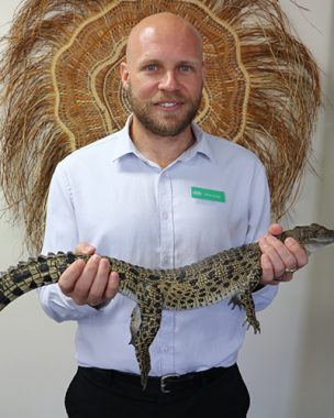CBB salary packaging team member Mitch holding a baby crocodile on a visit to an organisation in the NT to tell them about CBB