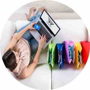 A lady sitting on the couch with a laptop doing online shopping with five shopping bags on the couch next to her
