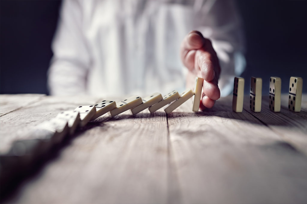 Businessman's hand stopping a line of dominos from falling