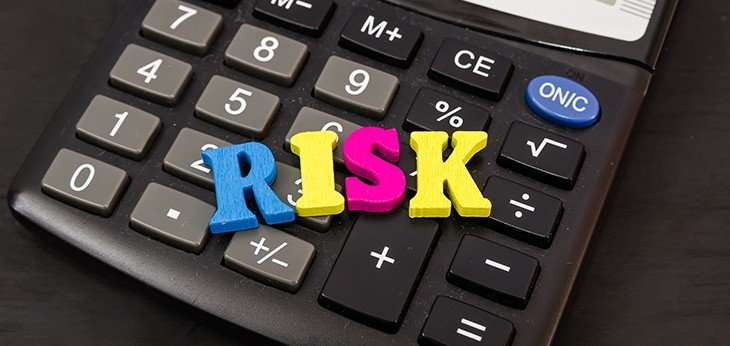 Calculator with the word risk in capital coloured wooden letters sittin on top of the calculator