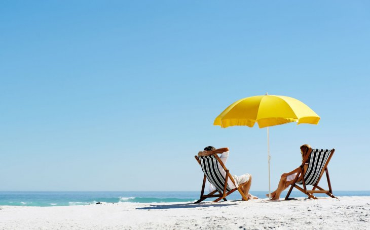 two people on holiday sitting on a beach under an umbrella