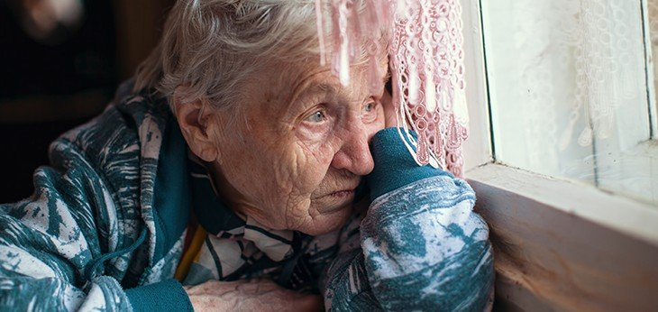 An image of an elderly lady staring hopelessly out of the window