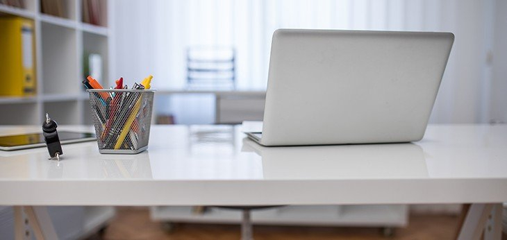 An open laptop next to a pot of pens, sitting on a white desk