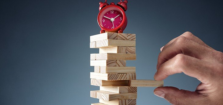 a person pulling out a Jenga brick with red alarm clock on top