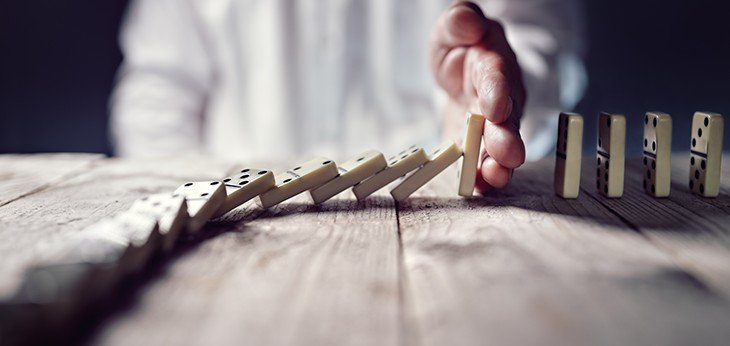 Dominos falling but stopped by a hand to prevent the rest of them falling