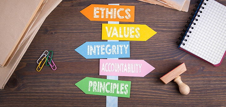 Flat sign post laying on a desk. The sign post has arrows facing alternatve ways with the words ethics, values, integrity, accountability and principles