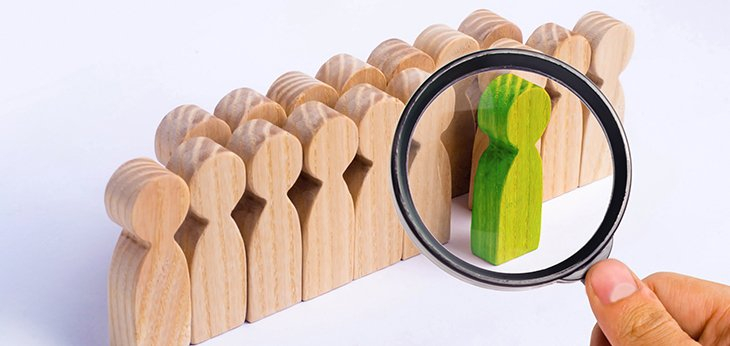 Green wooden figure with magnifying glass in front and white figures in the background